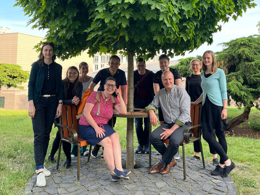 KI generiert: Das Bild zeigt eine Gruppe von Personen, die in einem hellen Raum mit großen Fenstern an langen Tischen sitzen und scheinbar einer Präsentation oder einem Vortrag folgen. Der Hauptinhalt des Bildes ist eine Versammlung oder ein Seminar in einem modernen, gut beleuchteten Innenraum.
