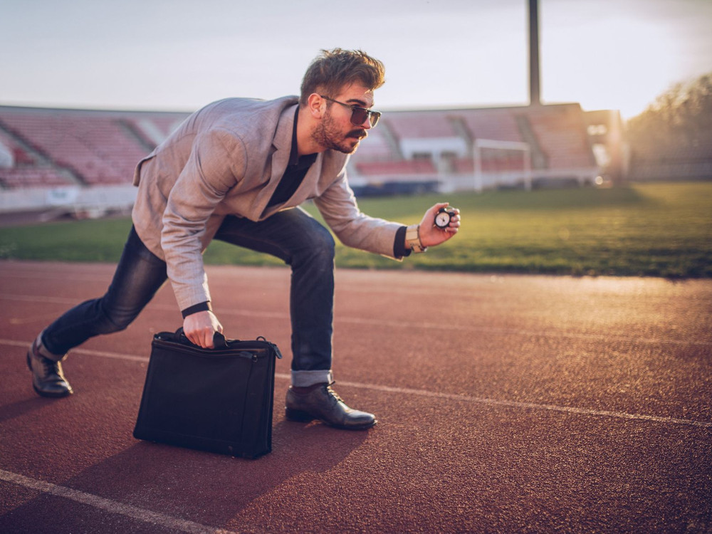 KI generiert: Das Bild zeigt einen Mann in einem Stadion, der sich in einer gebückten Haltung befindet und eine Stoppuhr in der Hand hält. Der Hauptinhalt des Bildes ist die Darstellung eines Sportlers oder Trainers, der möglicherweise eine Zeitmessung während eines Trainings oder Wettbewerbs durchführt.