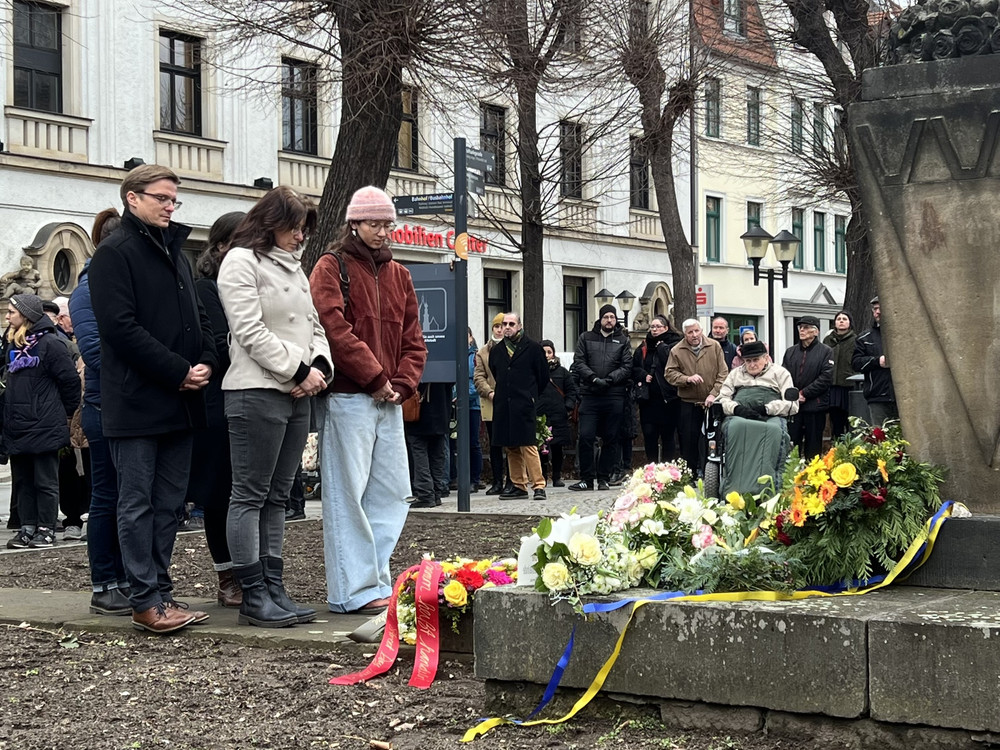 KI generiert: Das Bild zeigt einen Mann, der eine Ausstellung besucht und sich Informationsplakate ansieht, die sich auf die deutsche Besatzung und lokale Rekrutierung beziehen. Der Hauptinhalt der Ausstellung scheint historische Konflikte und Ereignisse während der deutschen Besatzung zu thematisieren.
