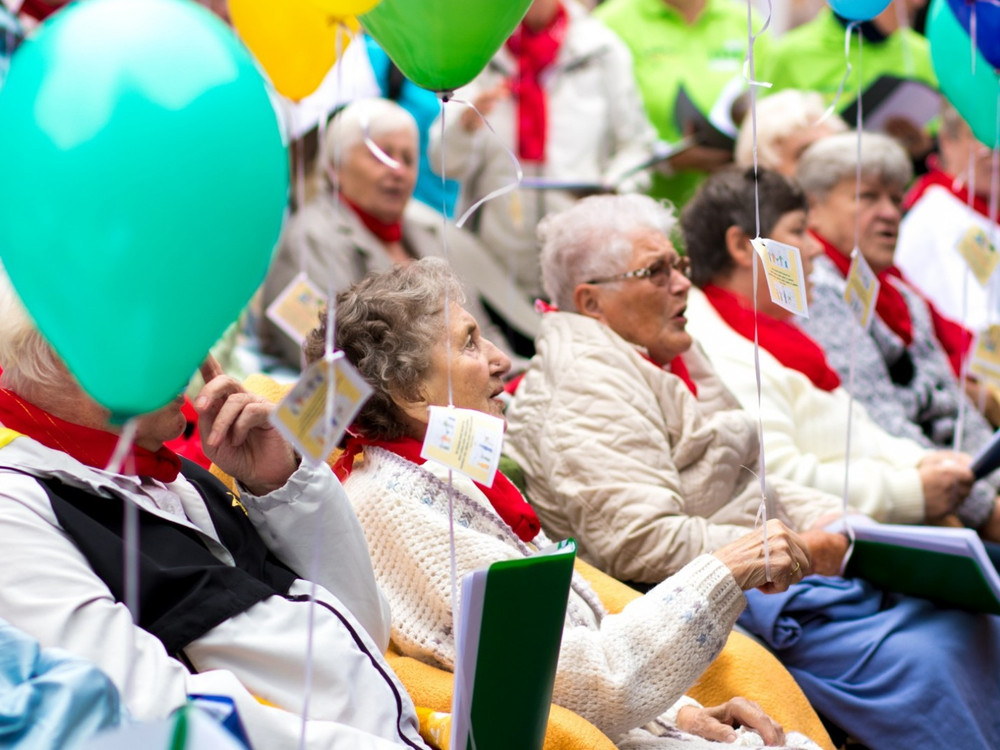 KI generiert: Das Bild zeigt eine Gruppe älterer Menschen, die auf Stühlen sitzen und an einer Veranstaltung teilnehmen, bei der sie bunte Ballons in den Händen halten. Der Hauptinhalt des Bildes ist die fröhliche und gesellige Atmosphäre unter den Senioren.