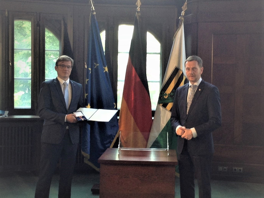 KI generiert: Das Bild zeigt eine Verleihungsurkunde in einem offenen, dunklen Etui. Die Urkunde ist an Herrn Sebastian Reißig für besondere Verdienste verliehen worden.