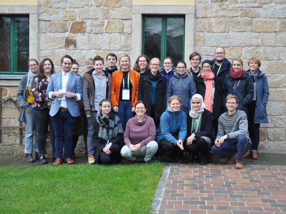 KI generiert: Das Bild zeigt eine Gruppe von Menschen, die vor einem steinernen Gebäude mit grünen Fenstern posieren. Der Hauptinhalt des Bildes ist die Gruppe von Personen, die gemeinsam ein Foto machen.
