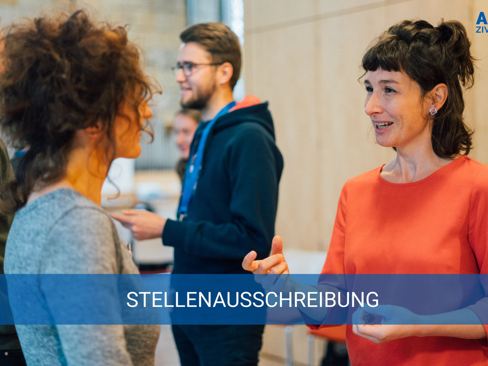KI generiert: Das Bild zeigt eine Gruppe von Personen, die sich in einer informellen Umgebung unterhalten, wobei eine Frau in einem orangen Pullover im Vordergrund steht und mit einer anderen Person spricht. Der Hauptinhalt des Bildes ist eine Stellenausschreibung, wie durch die Textzeile "STELLENAUSSCHREIBUNG" angezeigt wird.