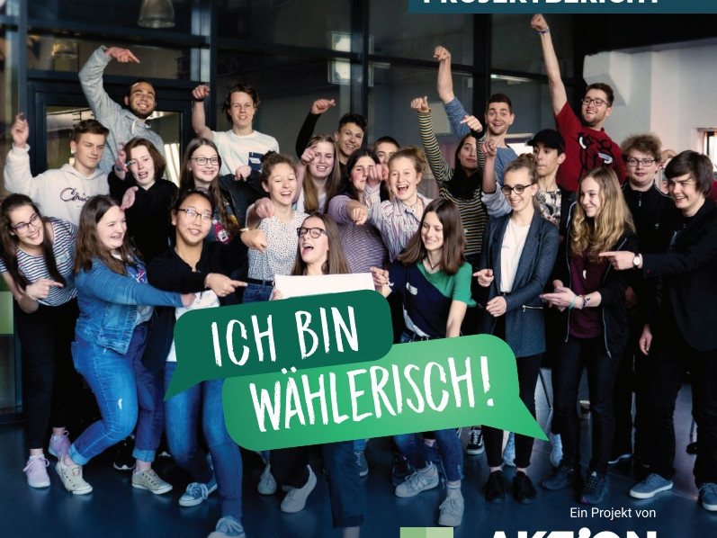 KI generiert: Das Bild zeigt eine Gruppe junger Menschen, die gemeinsam ein Banner mit der Aufschrift "ICH BIN WÄHLERISCH!" halten und dabei fröhlich und engagiert wirken. Es handelt sich um einen Projektbericht der "Aktion Zivilcourage" in Zusammenarbeit mit der Sächsischen Landeszentrale für politische Bildung.