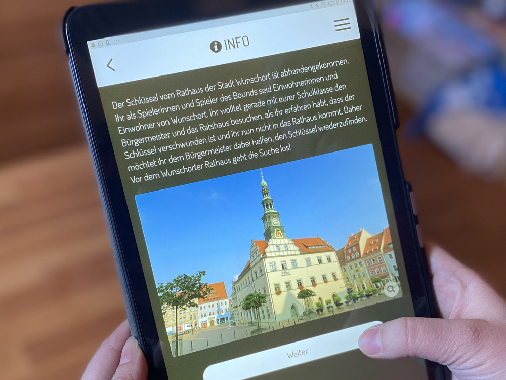 KI generiert: Das Bild zeigt eine Person, die ein Smartphone hält, auf dem ein Foto einer malerischen Stadt mit historischen Gebäuden und einem markanten Rathaus mit Uhrturm zu sehen ist. Der Hauptinhalt des Bildes ist die auf dem Smartphone angezeigte Stadtansicht.