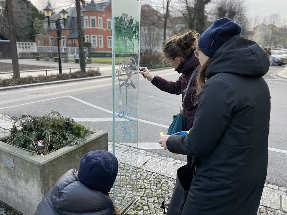 KI generiert: Das Bild zeigt eine Collage aus drei verschiedenen Ansichten: Einem mehrstöckigen Gebäude mit vielen Fenstern, einer Glasfläche mit der Aufschrift "Herr- und Pflegeanstalt" und einem Ausschnitt eines Turms mit Bäumen im Vordergrund. Der Hauptinhalt des Bildes scheint sich auf historische oder institutionelle Gebäude zu beziehen.