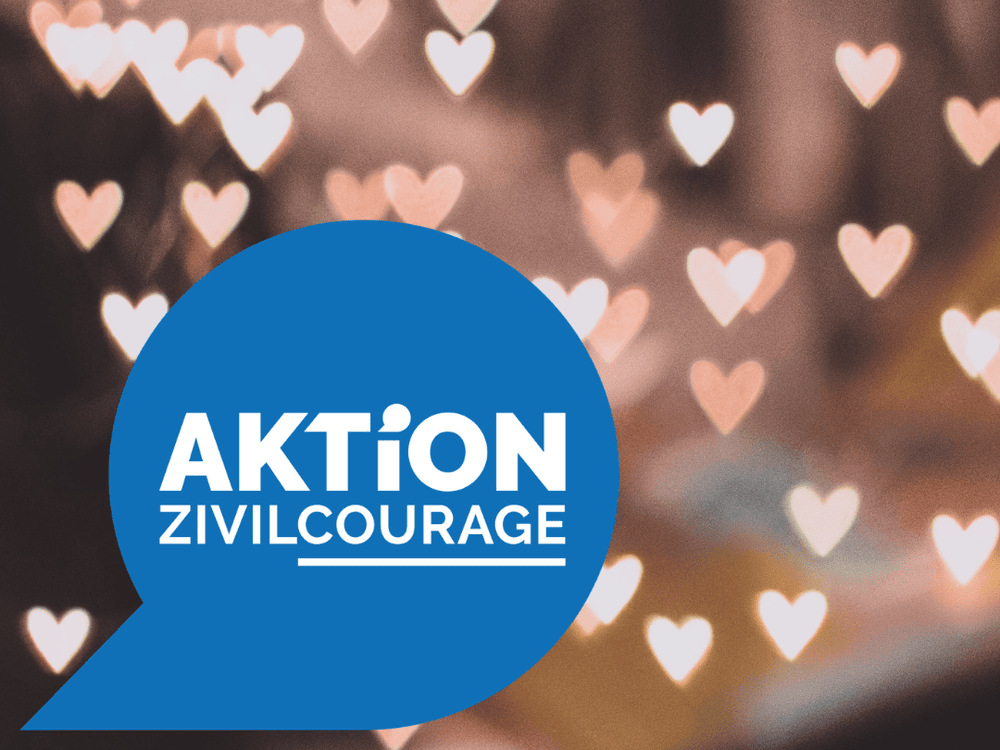 KI generiert: Das Bild zeigt ein Logo mit der Aufschrift "AKTION ZIVILCOURAGE" auf einem blauen Hintergrund. Im Hintergrund sind unscharf bunte Lichter und Herzformen zu erkennen.