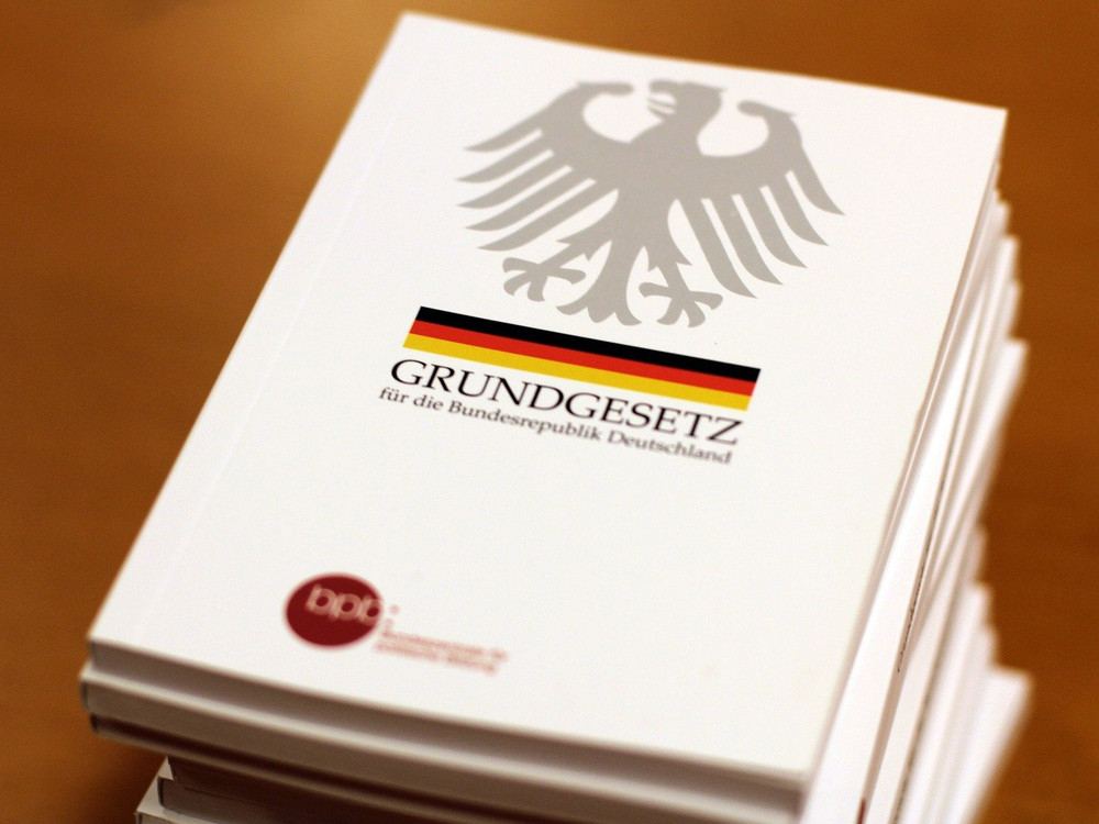 KI generiert: Das Bild zeigt ein Stapel von Dokumenten mit dem Aufdruck "GRUNDGESETZ für die Bundesrepublik Deutschland" und dem Bundesadler. Der Hauptinhalt des Bildes ist das Grundgesetz, die Verfassung der Bundesrepublik Deutschland.