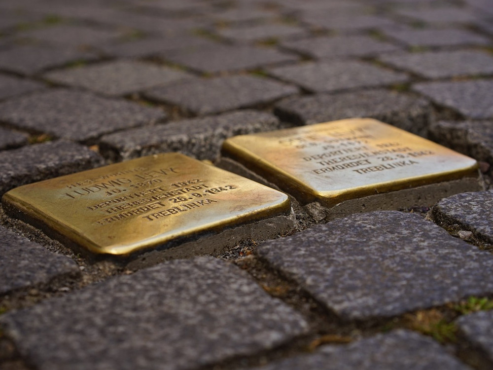 KI generiert: Das Bild zeigt zwei goldfarbene Stolpersteine, die in ein gepflastertes Gehwegfeld eingebettet sind. Diese Steine sind Teil eines Projekts zur Erinnerung an Opfer des Nationalsozialismus.