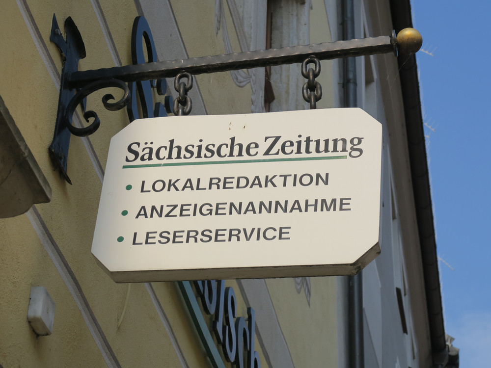 KI generiert: Das Bild zeigt ein modernes, mehrstöckiges Gebäude mit vielen Fenstern und einer Fassade aus hellen Paneelen. Im Vordergrund ist ein Verkehrsschild zu sehen, das auf ein Parkverbot hinweist. Der Hauptinhalt des Bildes ist das Gebäude.