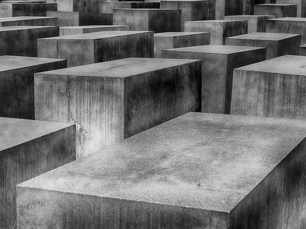 KI generiert: Das Bild zeigt das Holocaust-Mahnmal in Berlin, auch bekannt als "Denkmal für die ermordeten Juden Europas". Es besteht aus zahlreichen grauen Betonblöcken unterschiedlicher Höhen, die in einem wellenförmigen Muster angeordnet sind, mit Bäumen im Hintergrund.