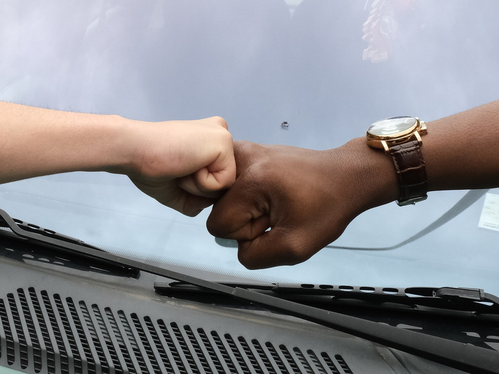 KI generiert: Das Bild zeigt zwei Personen, die sich mit ihren Fäusten begrüßen, wobei eine der Personen eine Armbanduhr trägt. Der Hauptinhalt des Bildes ist der Fauststoß als Geste der Begrüßung oder des Respekts.