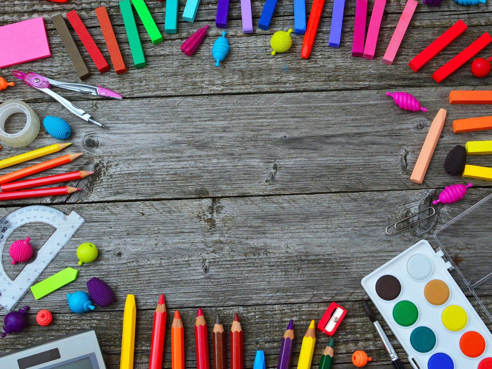 KI generiert: Das Bild zeigt eine bunte Ansammlung von Schul- und Bastelutensilien wie Stifte, Klebestift, Schere, Radiergummis und geometrische Formen auf einem rustikalen Holzhintergrund. Der Hauptinhalt des Bildes sind die verschiedenen farbenfrohen Gegenstände, die kreatives Arbeiten und Lernen symbolisieren.