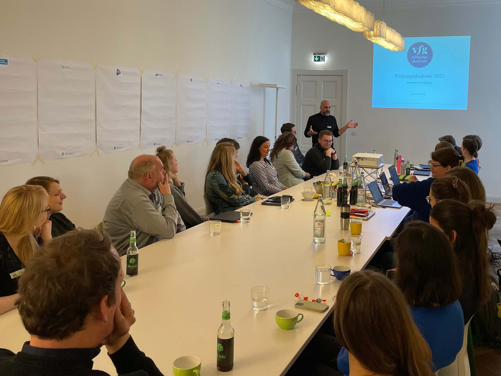KI generiert: Das Bild zeigt eine Gruppe von Personen, die vor einer Wand mit vielen bunten Notizzetteln posieren. Der Hauptinhalt des Bildes ist eine Team- oder Gruppenfotografie, möglicherweise im Rahmen eines Workshops oder einer Brainstorming-Sitzung.