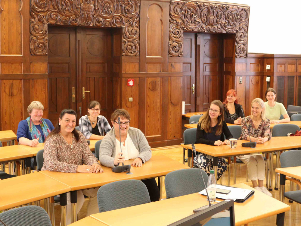 KI generiert: Das Bild zeigt eine Gruppe von Personen, die in einem Konferenzraum an langen Tischen sitzen. Der Hauptinhalt des Bildes ist eine Besprechung oder ein Seminar in einem formellen Umfeld.