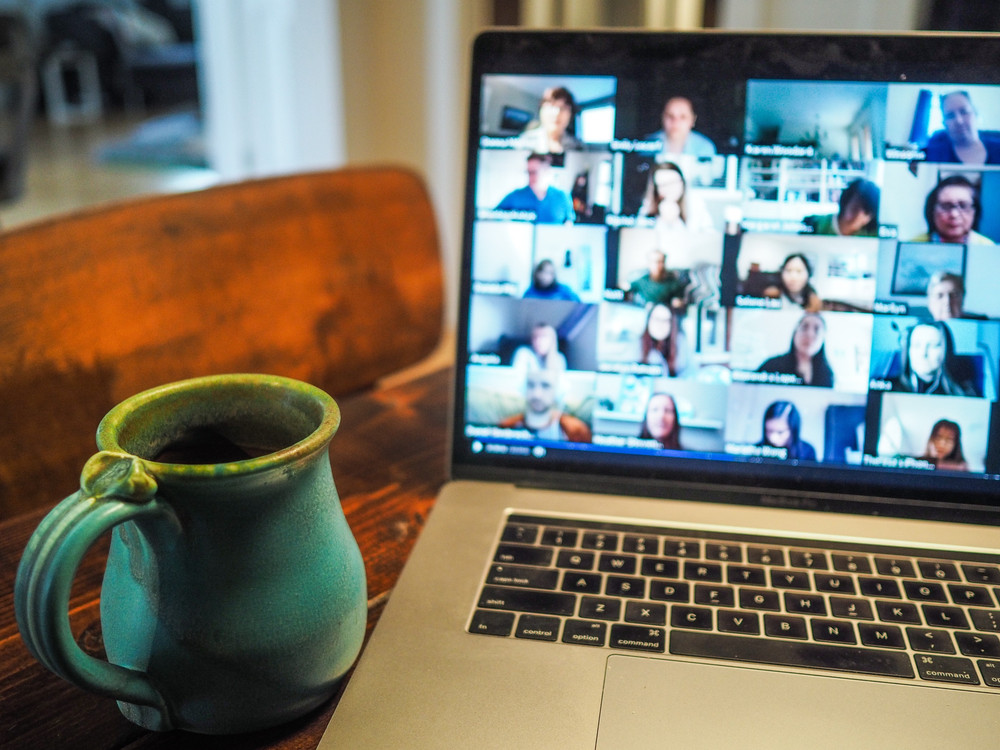 KI generiert: Das Bild zeigt einen Laptop mit einer laufenden Videokonferenz auf dem Bildschirm und eine grüne Tasse daneben. Der Hauptinhalt des Bildes ist die Darstellung einer virtuellen Besprechung oder eines Online-Meetings.